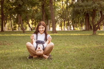 A young mother sits with her son, a boy in a lotus position in a park on a lawn, in the summer. Play, laughing baby. Sunset sun, life style. A woman is dressed in a denim overall. Family look.