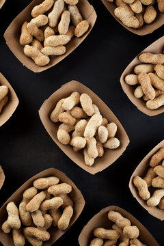 Peanuts with shell in disposable cardboard boxes on a black table.