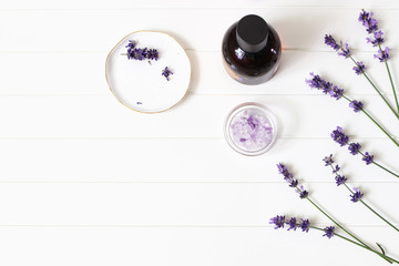 Styled summer beauty composition. Essential, massage oil, purple lavender flowers and bath salt on white wooden table background. Organic herbal cosmetics, spa concept. Empty space, flat lay, top view