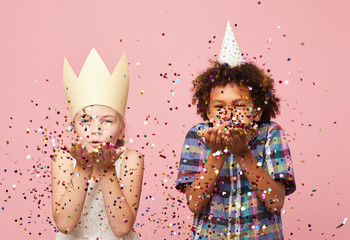 Waist up portyrait of two children blowing glitter at camera while standing against pink...
