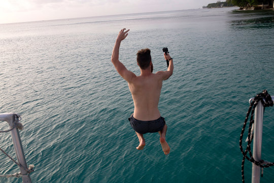 Man jumps into ocean holding selfie camera