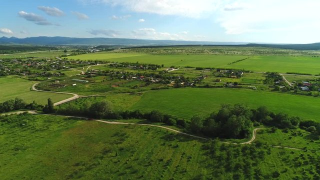 Aerial view of small village surrounded by green fields and meadows against blue cloudy sky in warm sunny day. Shot. Picturesque countryside view