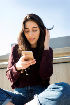 Young Woman Sitting Outside Texting On Her Phone