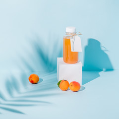 Composition of peach juice on pedestal and fresh apricots, palm branch shadow