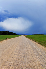 field, rural, gravel road covered with dust in the middle of a green field, before a thunderstorm, vertical photo.
