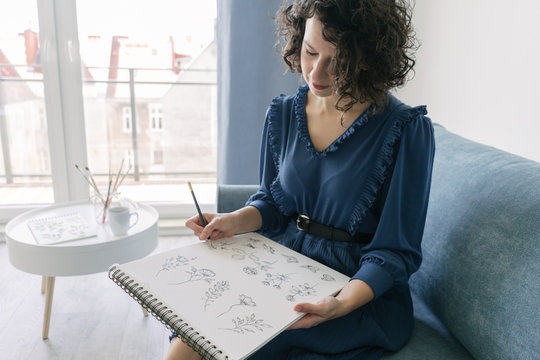 Elegant woman sitting on a sofa drawing on a notebook at home