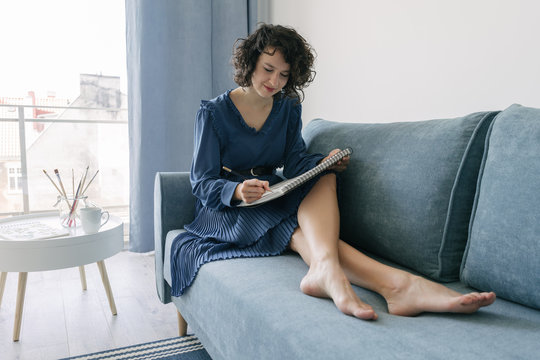 Elegant woman sitting on a sofa drawing on a notebook at home