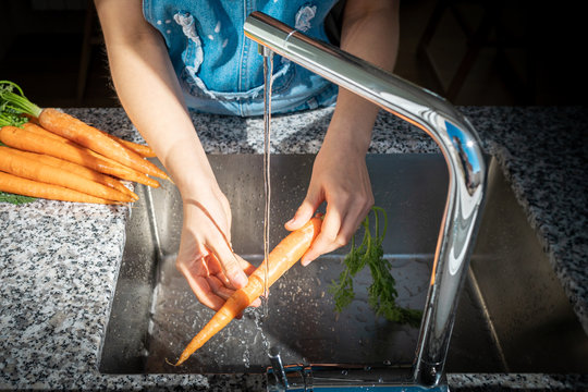 Hands of unrecognizable female washing ripe carrot under clean water over sink at home