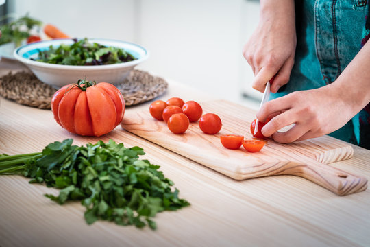 Anonymous woman cutting tomatoes while cooking healthy salad in kitchen
