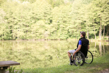 Happy and young disabled or handicapped man sitting on a wheelchair looking at beautiful lake in nature.