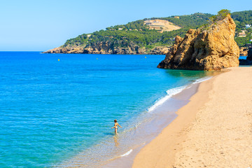 Fototapeta na wymiar Unidentified young woman walking into sea water on beautiful beach in Cala Moreta, Costa Brava, Spain