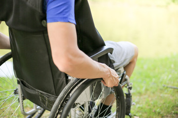 Young disabled or handicapped man sitting on a wheelchair in nature turning and holding wheels.