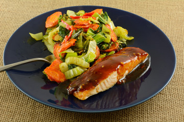 Baked salmon fish fillet with teriyaki sauce and vegetables on blue plate with fork