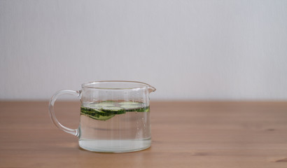 jug of lemonade and water sliced cucumbers and lemon on wooden table close up with blurred background