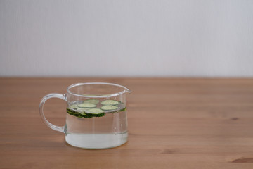 jug of lemonade and water sliced cucumbers and lemon on wooden table close up with blurred background