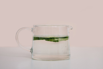 pitcher of lemonade and water sliced cucumbers and lemon on white table close-up with blurred background