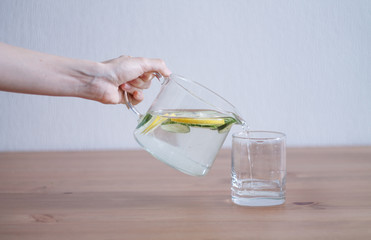 pitcher of lemonade and water holds hand sliced cucumbers and lemon on wooden table and blue table background close up with blurred background