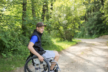 Fototapeta premium Happy and young disabled or handicapped man sitting on a wheelchair in nature turning wheels on a walking road at a beautiful sunny day