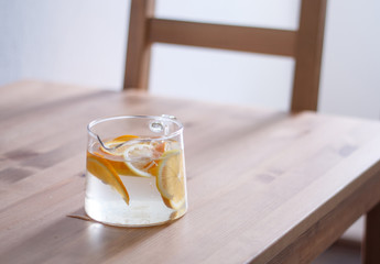 pitcher with lemonade and water sliced oranges and lemon on wooden table and coral and blue table background close up with blurred background