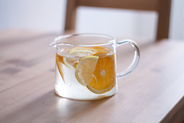 pitcher with lemonade and water sliced oranges and lemon on wooden table and coral and blue table background close up with blurred background
