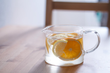 pitcher with lemonade and water sliced oranges and lemon on wooden table and coral and blue table background close up with blurred background