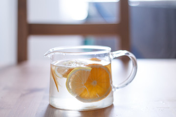 pitcher with lemonade and water sliced oranges and lemon on wooden table and coral and blue table background close up with blurred background
