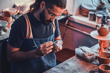Diligent pensive man in glasses at his pottery workshop is workig for new project.
