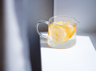 pitcher with lemonade and water sliced oranges and lemon on white table close-up with blurred background