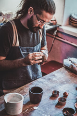 Diligent pensive man in glasses at his pottery workshop is workig for new project.