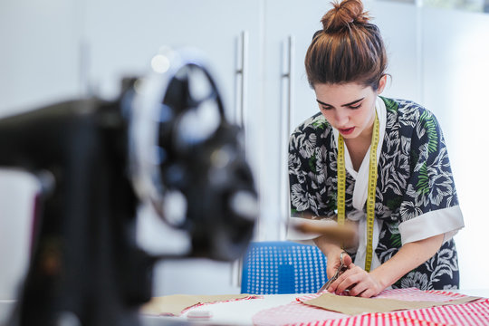 Teenage girl student practicing sewing on modern machine in cozy workshop