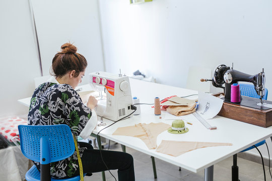 Teenage girl student practicing sewing on modern machine in cozy workshop