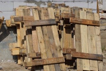 a pile of brown pallets of wooden planks outside against the wall
