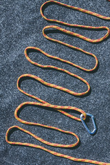 Bright orange rope with a small carabiner on a texured roofing felt surface with many small grey stones