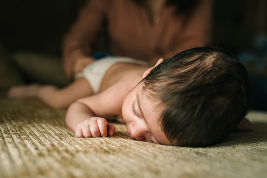 Cute little innocent newborn baby in back lying on sofa at home with mum behind