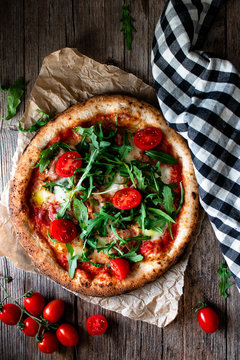 From above delicious pizza with tomato and salad placed with checkered towel on wooden background