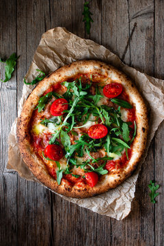 From above delicious pizza with tomato and salad placed with checkered towel on wooden background