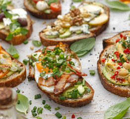Assorted open faced sandwiches, Open avocado sandwiches made of slices of sourdough bread with various toppings  on a white wooden table. Delicious and nutritious breakfast