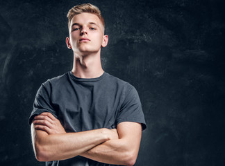 Young arrogant male is looking to the camera crossed his hands over dark background.