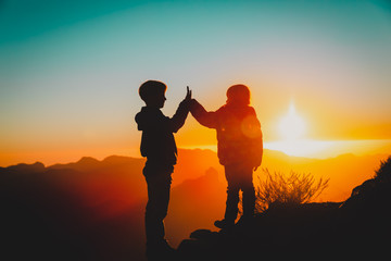 Fototapeta na wymiar Silhouettes of happy boy and girl hiking at sunset mountains