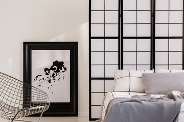 Fancy industrial armchair next to comfortable bed in bright interior