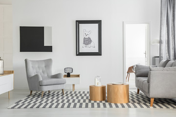 Comfortable grey armchair in elegant living room interior with white furniture and two wooden...