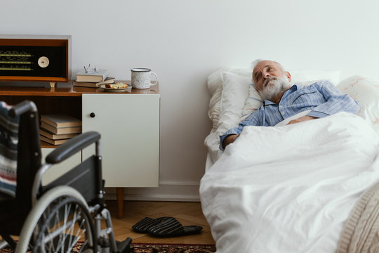 Sick elderly man wearing blue pajama lying in bed at nursing home