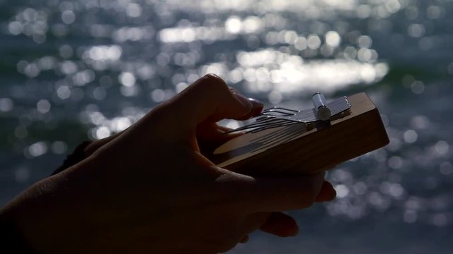 Silhouette of a woman hands with a small musical instrument, fantastic shining ocean on the background.