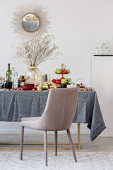 Stylish chair next to dining table with food, fruits and flowers