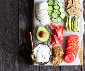 Healthy breakfast ingredients: smoked salmon, liver pate, cucumber, tomato, avocado, mozzarella and cream cheese, multigrain crackers.  Breakfast served with coffee and milk. Healthy snacks.