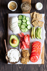 Healthy breakfast ingredients: smoked salmon, liver pate, cucumber, tomato, avocado, mozzarella and cream cheese, multigrain crackers.  Breakfast served with coffee and milk. Healthy snacks.