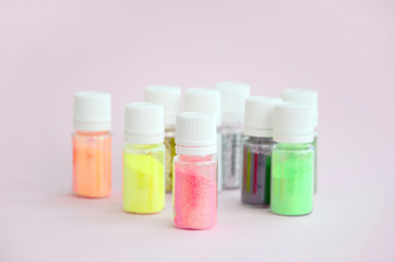 Colorful glitters lies on pastel pink background. Many round jars with multi-colored bright sparkles for nail polish