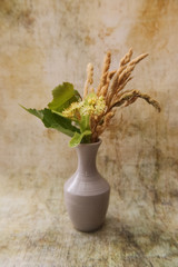 White vase with a bouquet of fragrant yellow flowers and leaves of linden and dried grass hedgehogs.