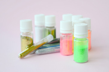 Colorful glitters lies on pastel pink background. Many round jars with multi-colored bright sparkles for nail polish