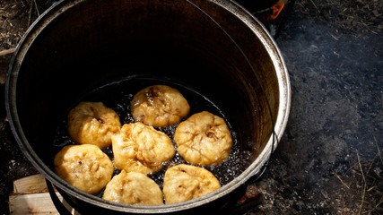 Cooking a national Russian, Bashkir, Tatar dish - belyashes in nature, in a cauldron on an open fire. Frying in oil. Picnic and barbecue